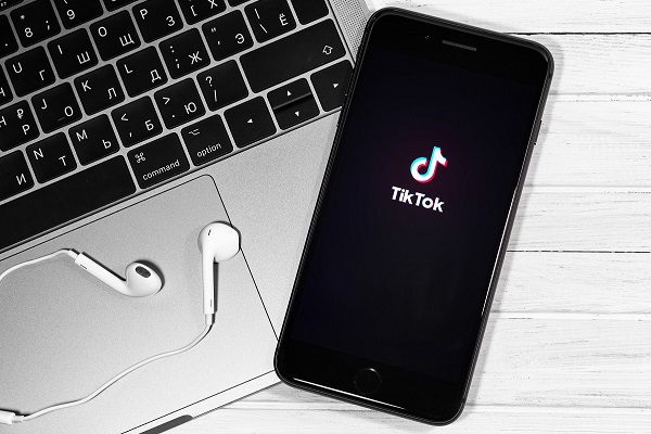 TikTok logo on the display iPhone, notebook and headphones Apple Earpods closeup. TikTok is app to create and share videos. Moscow, Russia - December 23, 2019